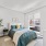 Model bedroom with queen bed, dresser on one side, bedside table with light and tree on the left